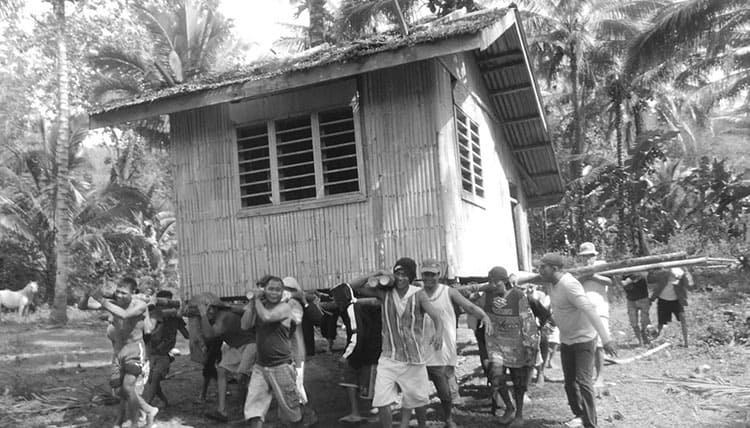 People moving a wooden house using wooden poles