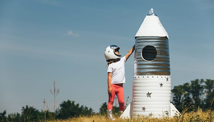 Happy child girl dressed in an astronaut costume playing with hand made rocket.